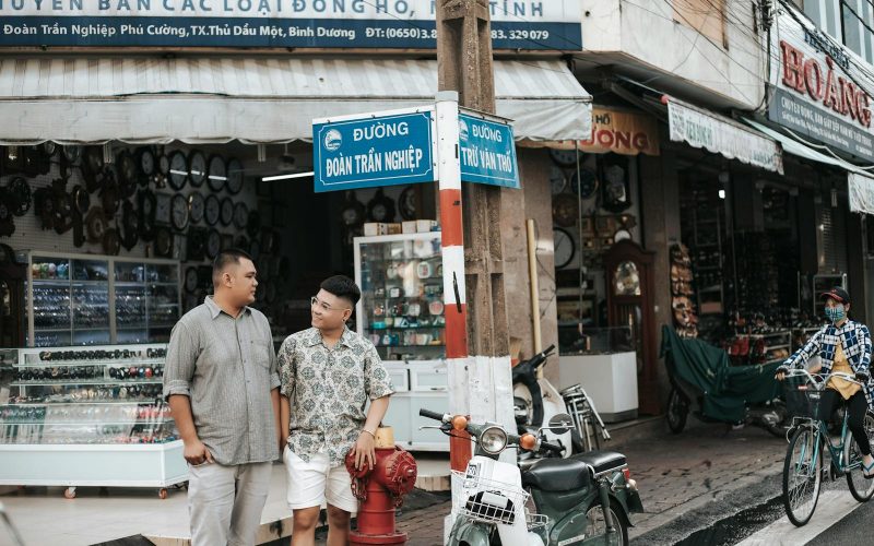 Two men talking beside motorbikes in a vibrant market street, showcasing local street life.