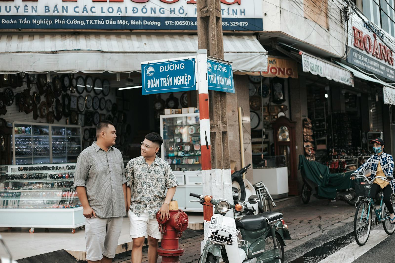 Two men talking beside motorbikes in a vibrant market street, showcasing local street life.