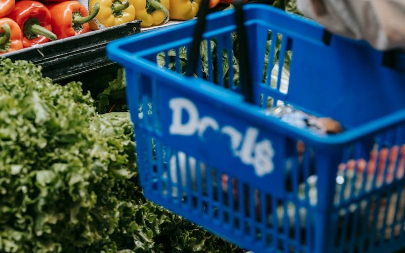 Side view of crop faceless buyer in casual clothes carrying shopping basket while choosing assorted colorful bell peppers in supermarket